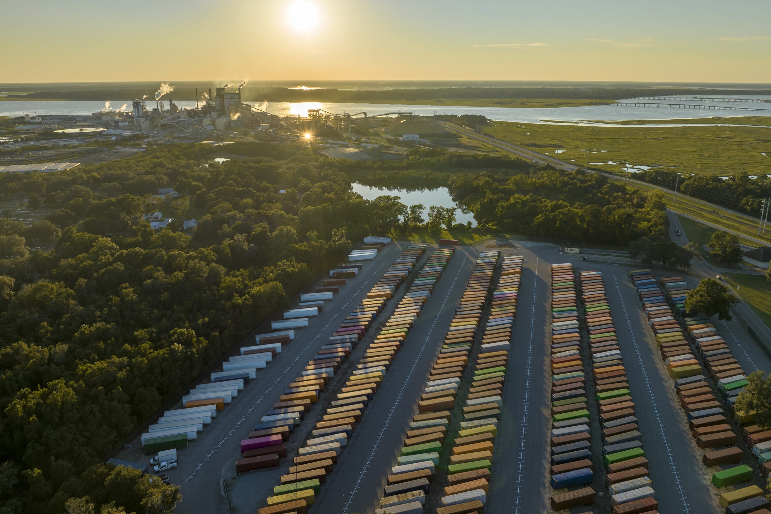 Large cargo container yard with many freight containers and big factory manufactory structure. Production and distribution of produced goods