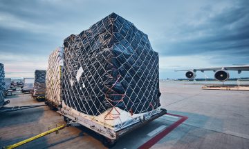 Cargo containers secured on a pallet at an airport, ready for air freight transportation, with an airplane in the background, emphasizing logistics and supply chain solutions.