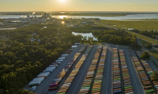 Aerial view of a large cargo container yard filled with various freight containers, showcasing a commitment to logistics and transportation services, with a backdrop of industrial facilities and a river, reflecting Smith Transport Solutions