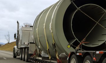 Truck transporting large cylindrical cargo on a highway, illustrating logistics for bulky goods in North America.