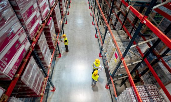Warehouse workers in safety gear organizing inventory on high shelves, emphasizing logistics and distribution services.
